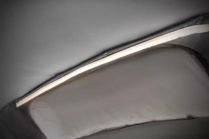 Gebogene graue Oberfläche mit schmalem, beleuchtetem weißen Streifen über einem hellen, gepolsterten Einsatz