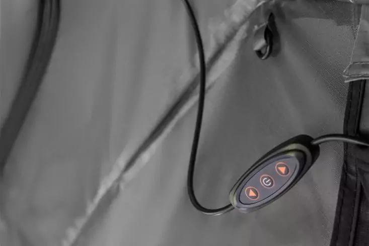 Schwarze ovale Fernbedienung mit drei orange beleuchteten dreieckigen Tasten an einem schwarzen Kabel, befestigt an grauem Stoff mit Naht und Reißverschluss