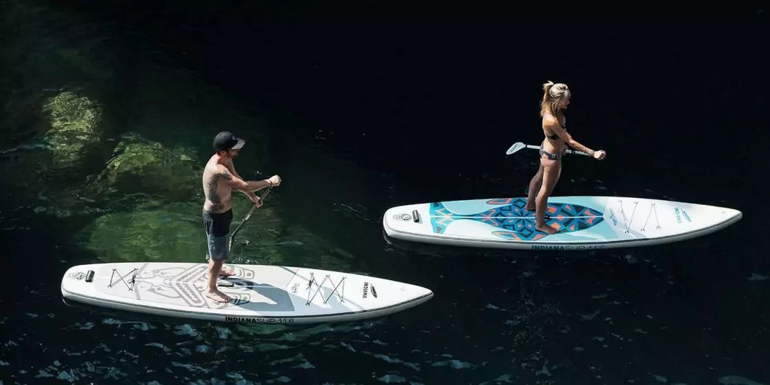 Zwei Personen auf Stand-up-Paddle-Boards auf dunklem Wasser, beide stehen und halten Paddel