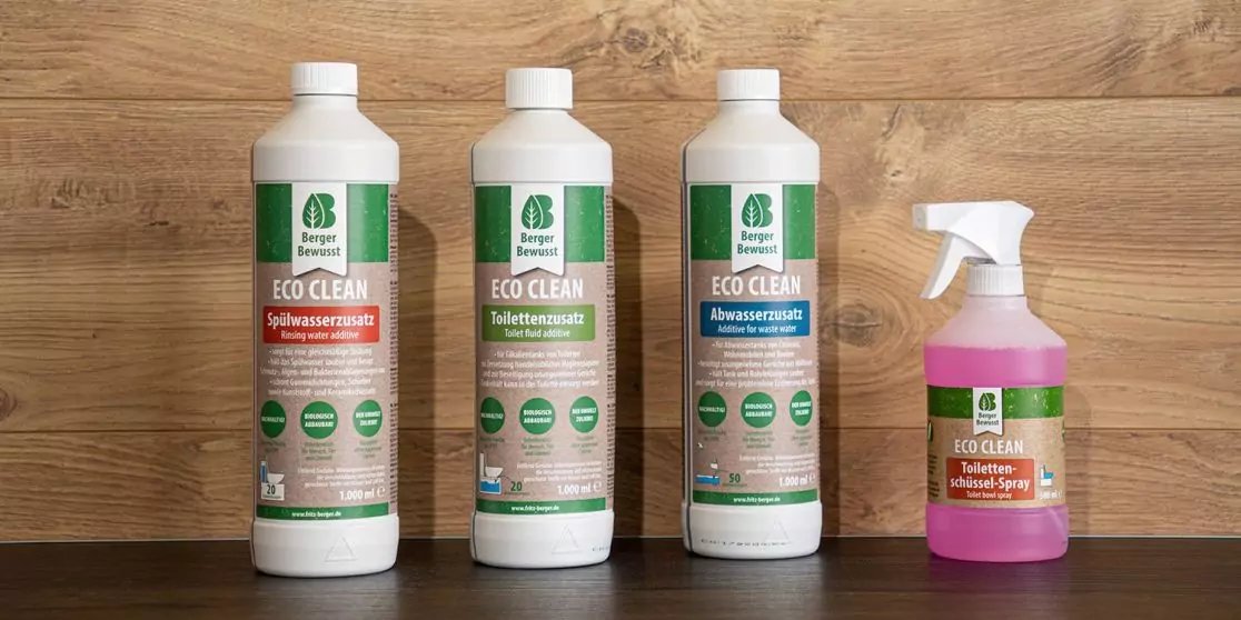 Drei wei&szlig;e Flaschen mit gr&uuml;nen Etiketten und eine kleine Spr&uuml;hflasche mit rosa Fl&uuml;ssigkeit auf einer Holzoberfl&auml;che vor einer Holzwand