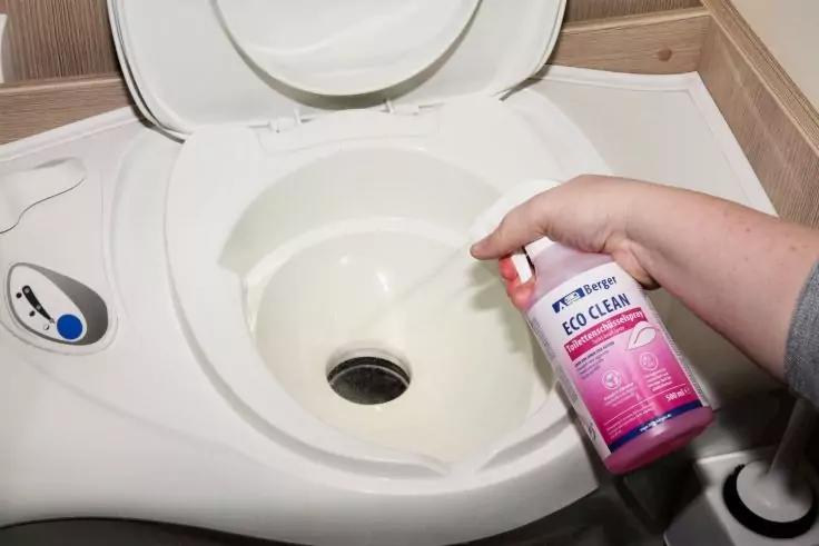 Ge&ouml;ffnete wei&szlig;e Toilettensch&uuml;ssel, rechts h&auml;lt eine Hand eine rosa-wei&szlig;e Flasche mit der Aufschrift 'ECO CLEAN'