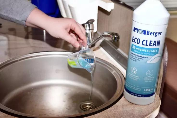Hand h&auml;lt ein kleines Glas unter einen laufenden Wasserhahn &uuml;ber einer Edelstahlsp&uuml;le; rechts steht eine gro&szlig;e wei&szlig;e Flasche mit blauem Etikett Berger ECO CLEAN