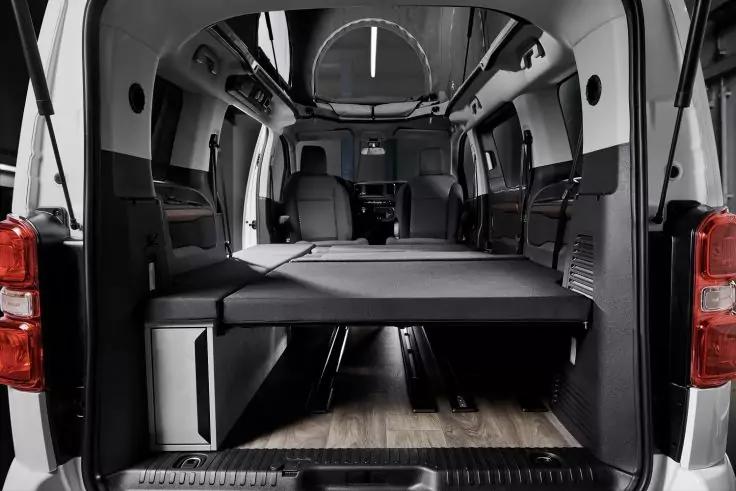 Offener Laderaum eines Vans mit flacher, gepolsterter Liegefl&auml;che, Stauraum darunter, zwei Vordersitzen und Deckenbeleuchtung