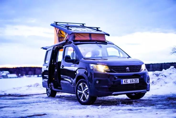 Dunkler Peugeot-Camper mit aufgeklapptem Aufstelldach, ge&ouml;ffneter Schiebet&uuml;r und eingeschalteten Scheinwerfern, auf schneebedecktem Boden geparkt