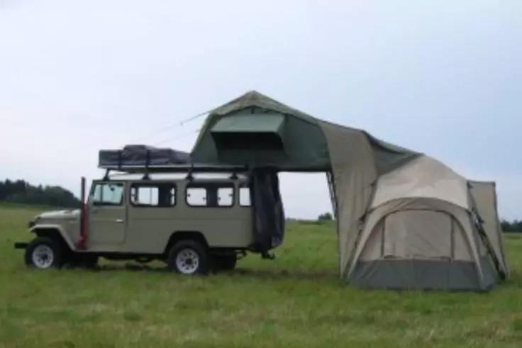 Gel&auml;ndewagen mit Dachzelt und seitlich angebautem Vorzelt auf einer Wiese, bew&ouml;lkter Himmel, keine Personen