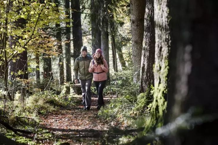 Zwei Personen in Jacken gehen auf einem Waldweg zwischen B&auml;umen