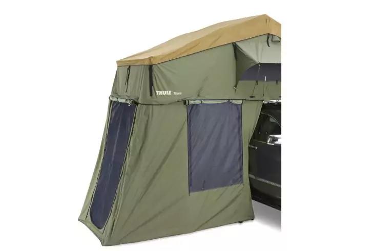 Gr&uuml;ner zelt&auml;hnlicher Anbau mit beigem Dach, zwei dunklen Fenster&ouml;ffnungen, rechts teilweise ein schwarzes Fahrzeug sichtbar