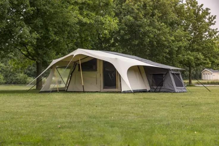 Gro&szlig;es beige-graues Zelt mit Vordach auf einer Grasfl&auml;che, im Hintergrund B&auml;ume