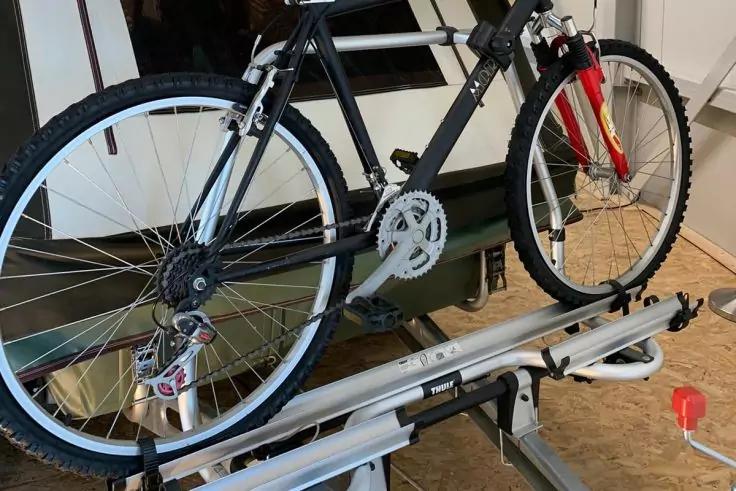 Schwarzes Fahrrad mit roter Gabel auf silberner Fahrradhalterung in einem Raum, sichtbar: Kettenbl&auml;tter, Kassette und R&auml;der