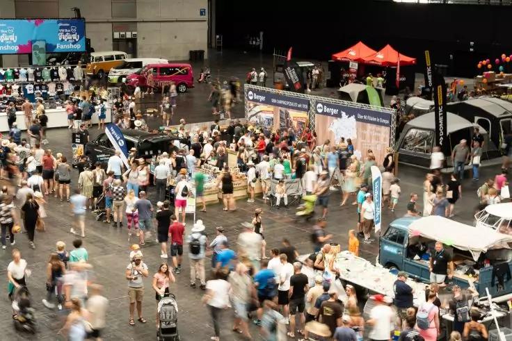 Gro&szlig;e Innenhalle mit vielen Personen, Messest&auml;nden, mehreren Lieferwagen und St&auml;nden, Vogelperspektive