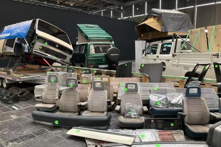 Mehrere beige Autositze, Armaturenbretter und Fahrzeugkarosserien in einer Halle