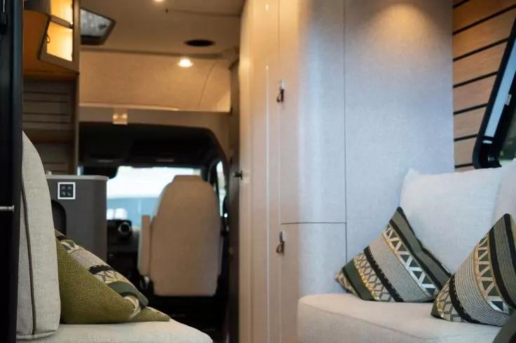 Innenraum eines Campers mit Sitzb&auml;nken, gemusterten Kissen, Schrankfronten und Blick zum Fahrerhaus