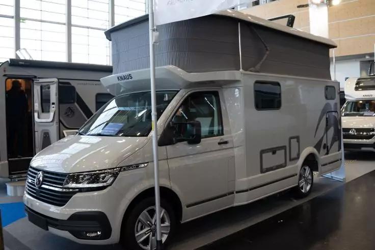 Wei&szlig;-graues Wohnmobil mit hochgeklapptem Aufstelldach, Seitenansicht in einer Messehalle, Metallpfosten im Vordergrund