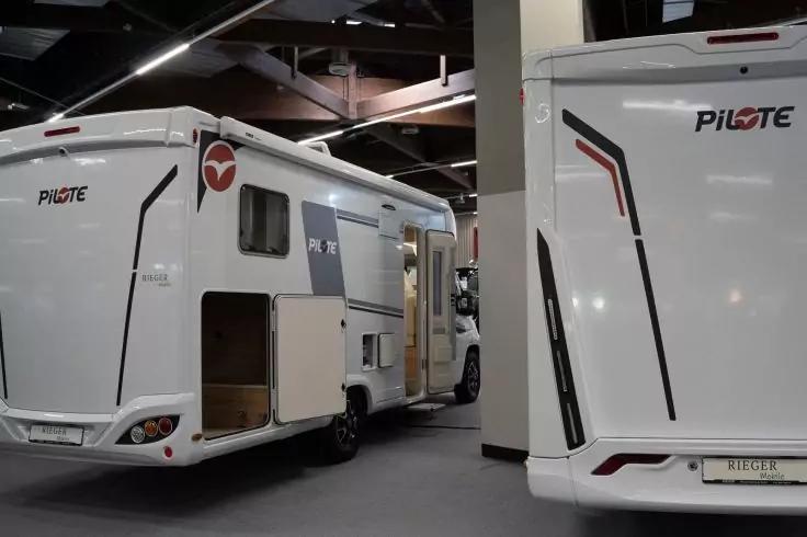 Zwei wei&szlig;e Wohnmobile in einer Halle, eines mit ge&ouml;ffneter Seitent&uuml;r und ge&ouml;ffneter Stauraumklappe, S&auml;ule dazwischen