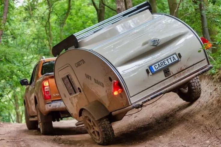 Pick-up auf unbefestigtem Waldweg mit kleinem silbernem Teardrop-Anh&auml;nger; Anh&auml;ngerheck schr&auml;g nach rechts, B&auml;ume im Hintergrund