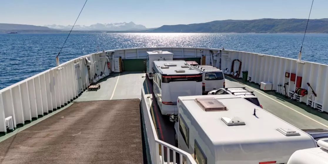 Heckdeck einer F&auml;hre mit mehreren Wohnmobilen, Meer mit Sonnenreflexion und fernen Bergen
