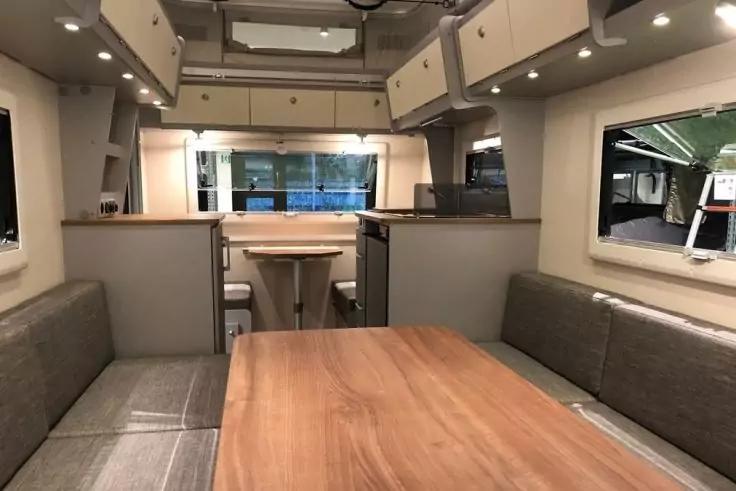 Innenraum mit mittigem Holztisch, gegen&uuml;berliegenden Polsterb&auml;nken, Ober- und Unterschr&auml;nken, Fenstern und Deckenbeleuchtung