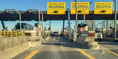 Mautstelle mit drei gelben &bdquo;TELEPASS&ldquo;-Schildern &uuml;ber Fahrspuren, ein Auto in der mittleren Spur, Schranken und Betonabsperrungen