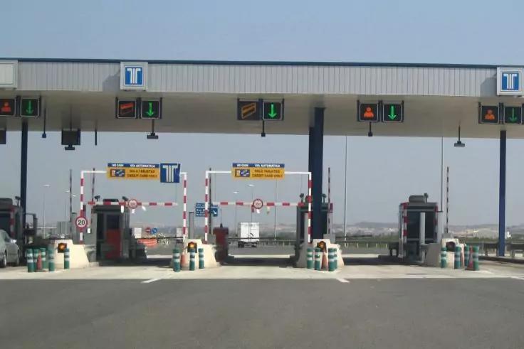 Mautstelle mit Vordach, mehreren Fahrspuren, Schranken, roten Kreuzen und grünen Pfeilen, einzelnen Fahrzeugen