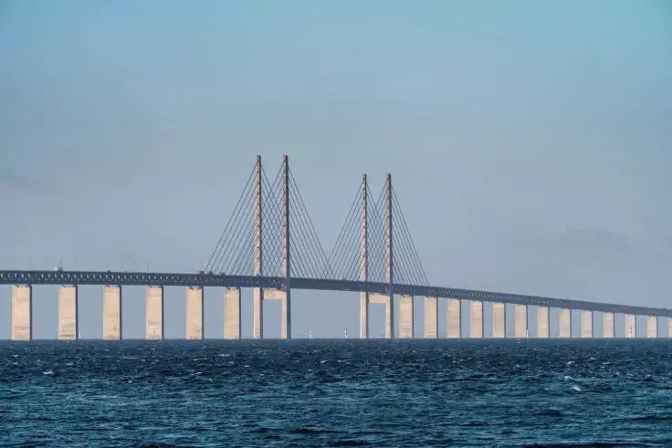 Lange Schrägseilbrücke mit mehreren Pylonen und aufgehängten Kabeln über einer Wasserfläche unter hellem Himmel