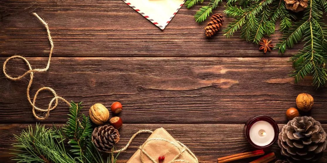 Holzbrett mit Tannenzweigen, Kiefernzapfen, Waln&uuml;ssen und Haseln&uuml;ssen, eingepacktes Geschenk mit Schnur, Kerze in Halter, Zimtstangen und Kordel