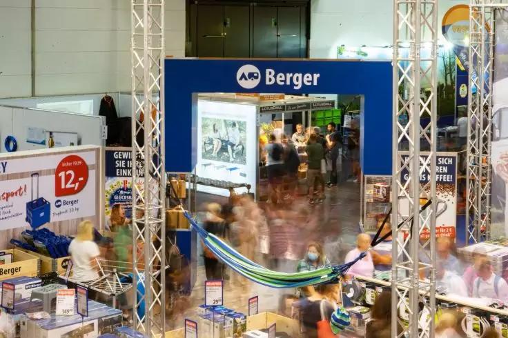 Blauer Portalrahmen mit Schriftzug "Berger", umgeben von weiteren St&auml;nden, Tischen und verschwommenen Personen in einer Halle