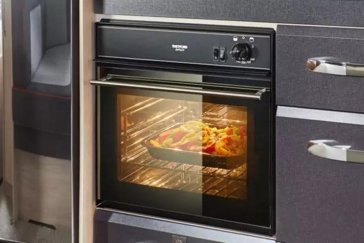 Einbaubackofen in dunkler K&uuml;chenzeile, geschlossene Glast&uuml;r, Innenlicht an, Backblech mit geschnittenem Gem&uuml;se