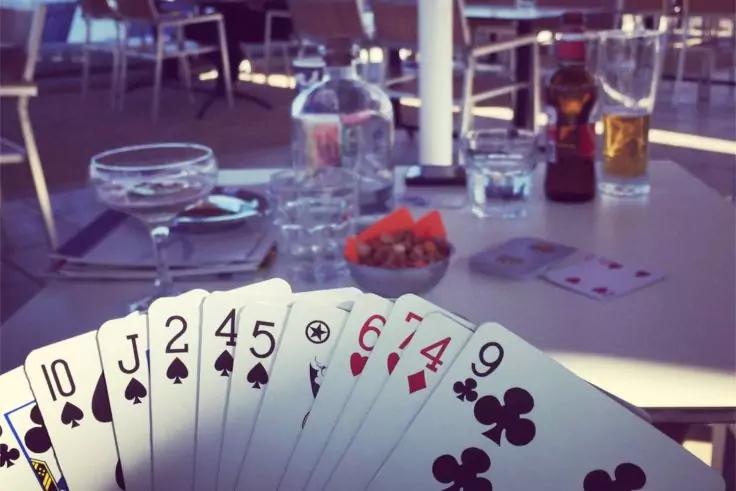 Gef&auml;cherte Spielkarten in einer Hand; im Hintergrund auf dem Tisch: ein Coup&eacute;glas, ein Wasserglas, eine Bierflasche mit Bierglas, ein Kerzenhalter, eine kleine Glasschale und eine Schale mit Cherrytomaten