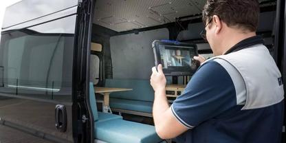 Ein Mann in Arbeitsweste steht in einem ge&ouml;ffneten Transporter und h&auml;lt ein Tablet; im Innenraum sind eine Sitzbank und Regale sichtbar