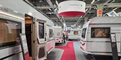 Gro&szlig;e Halle mit mehreren nebeneinander stehenden Wohnwagen, roter Mittelgang, h&auml;ngende Schilder und Deckenbeleuchtung