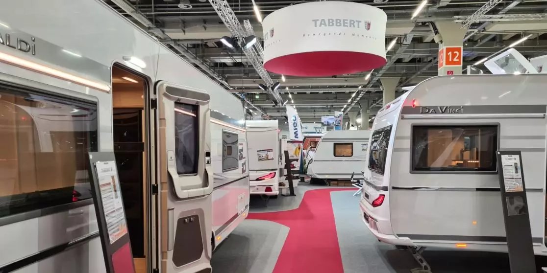 Gro&szlig;e Halle mit mehreren nebeneinander stehenden Wohnwagen, roter Mittelgang, h&auml;ngende Schilder und Deckenbeleuchtung