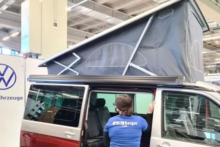 Rotes Wohnmobil mit aufgeklapptem Aufstelldach in einer Halle; seitliche Schiebet&uuml;r offen; Person in blauem Shirt steht an der T&uuml;r