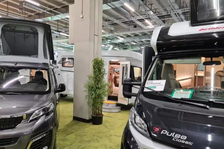 Innenraum mit mehreren Wohnmobilen, gr&uuml;ner Teppichboden, S&auml;ule mit Topfpflanze, sichtbare Deckenbeleuchtung