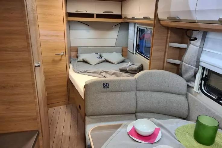 Innenraum eines Wohnmobils mit Heckbett und Kissen, Sitzecke und Tisch mit Teller, Sch&uuml;ssel und gr&uuml;nem Becher, Holzvert&auml;felung und Fenster