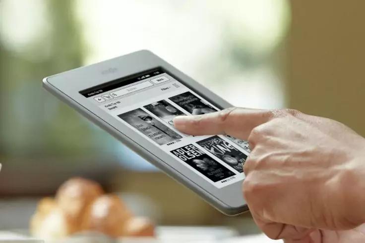 Hand ber&uuml;hrt mit Zeigefinger den Bildschirm eines wei&szlig;en Tablets; auf dem Bildschirm sind Miniaturbilder in einem Raster; unscharfer Hintergrund mit Geb&auml;ck