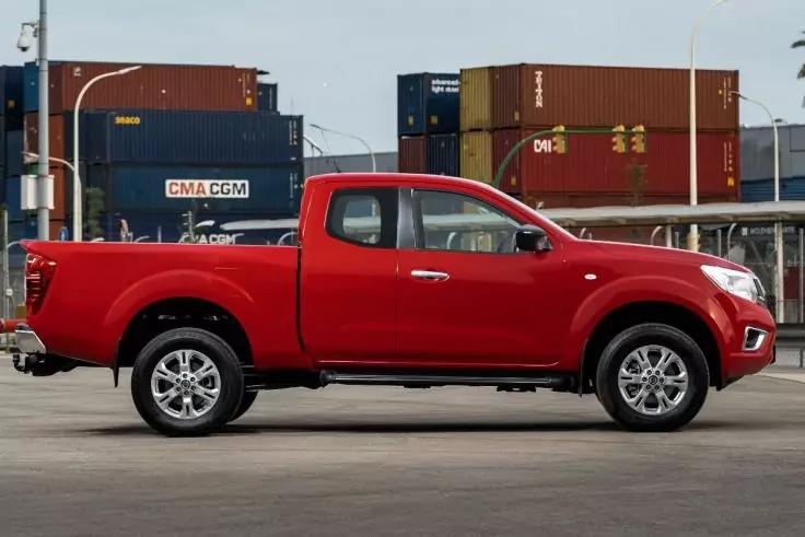 Roter Pick-up im Seitenprofil auf asphaltiertem Untergrund, im Hintergrund gestapelte Frachtcontainer und Stra&szlig;enlaternen