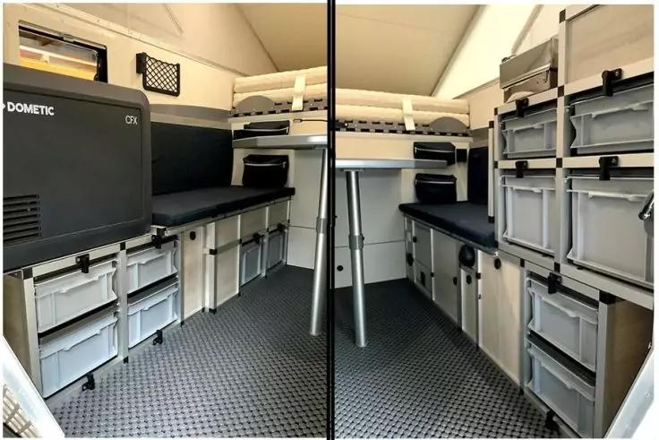 Innenraum mit langen Arbeitsfl&auml;chen links und rechts, gepolsterten oberen Liegefl&auml;chen, gestapelten Kunststoffboxen in Regalen, K&uuml;hlger&auml;t mit Aufschrift "Dometic" links, zentraler Metallst&uuml;tzstange und dunkel strukturiertem Boden