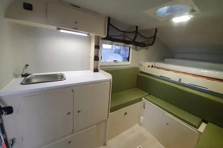 Wei&szlig;er Innenraum mit Sp&uuml;le und Arbeitsfl&auml;che links, gr&uuml;ne gepolsterte Sitzbank rechts, kleines rechteckiges Fenster hinten, Deckenluke, Schr&auml;nke und Stauraum