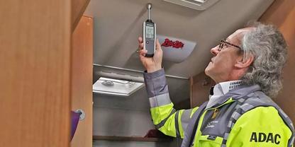 Person mit gelber Warnjacke mit Aufdruck "ADAC" im Innenraum eines Wohnmobils, h&auml;lt ein Handger&auml;t an die Decke