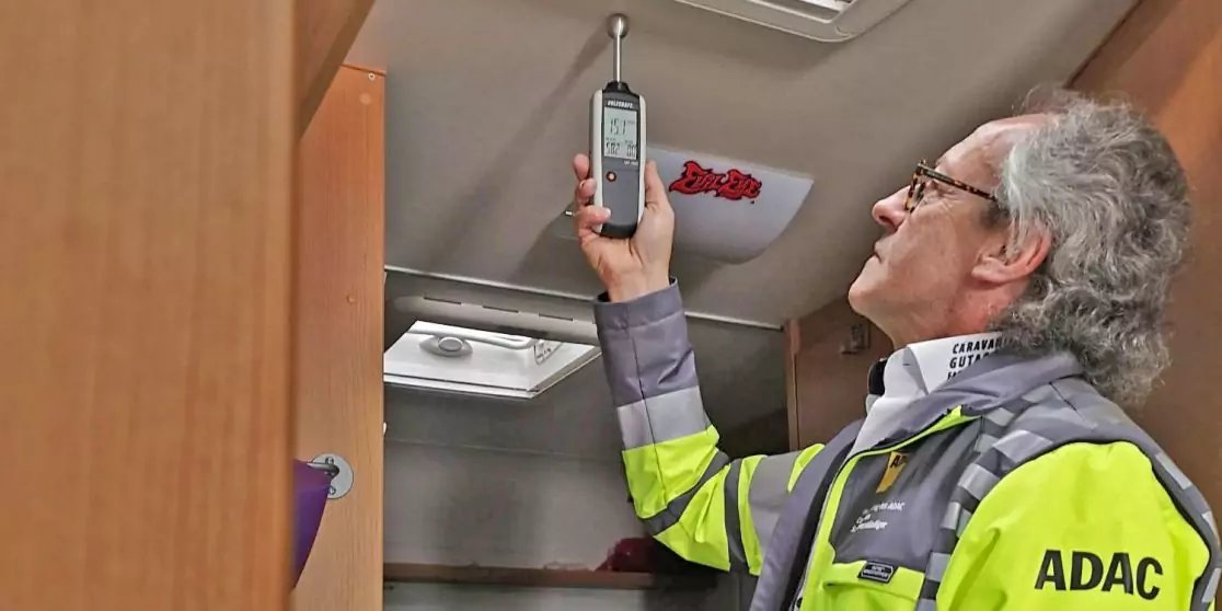 Person mit gelber Warnjacke mit Aufdruck "ADAC" im Innenraum eines Wohnmobils, h&auml;lt ein Handger&auml;t an die Decke