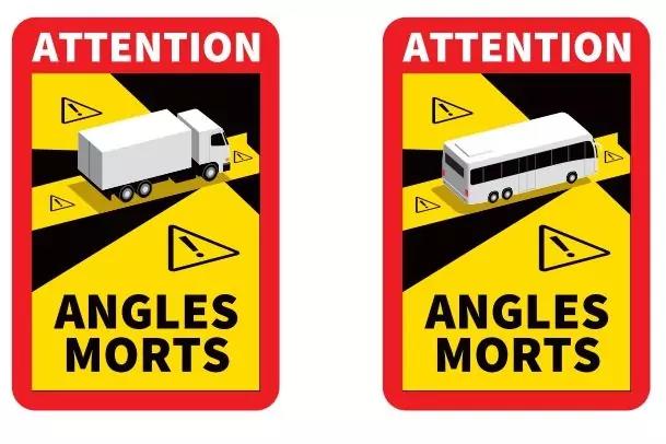 Zwei rechteckige Warnschilder mit rotem Rand. Oben steht "ATTENTION". Linkes Schild zeigt einen wei&szlig;en Lkw auf gelb-schwarzem diagonalen Hintergrund mit Warndreiecken. Rechtes Schild zeigt einen wei&szlig;en Bus auf demselben Hintergrund. Unten steht "ANGL