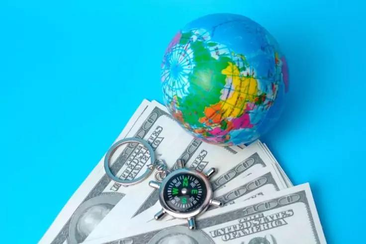 Kleiner bunter Globus, US-Dollar-Scheine, Kompass und Lupe auf blauem Hintergrund