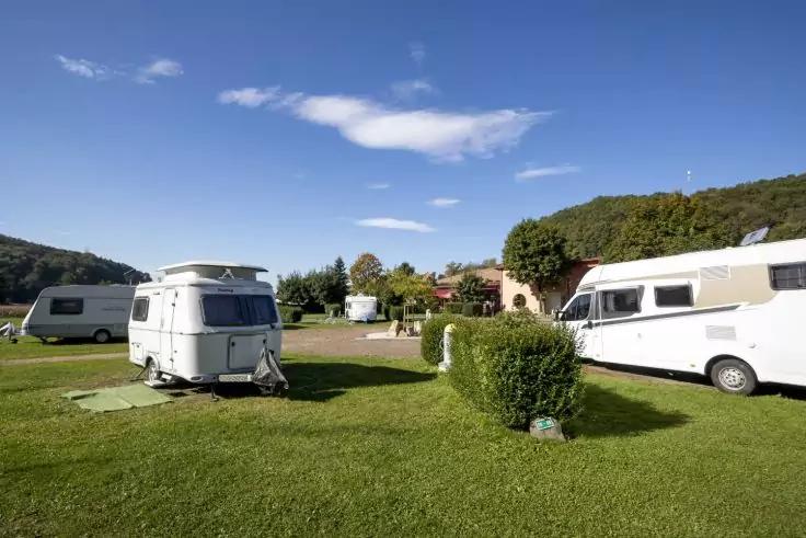 Mehrere Wohnwagen und ein Wohnmobil auf Rasen, blauer Himmel, B&auml;ume, H&uuml;gel und Geb&auml;ude im Hintergrund