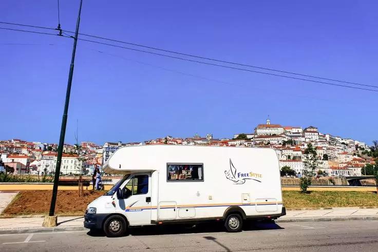Wei&szlig;es Wohnmobil am Stra&szlig;enrand, im Hintergrund eine auf einem H&uuml;gel liegende Stadt mit wei&szlig;en Geb&auml;uden, blauer Himmel, Strommast und Leitungen