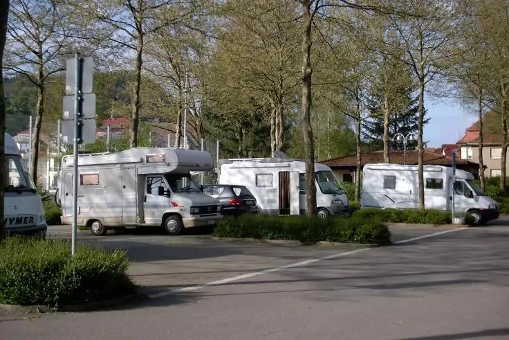 Mehrere Wohnmobile auf einem Parkplatz, im Hintergrund B&auml;ume und Wohnh&auml;user