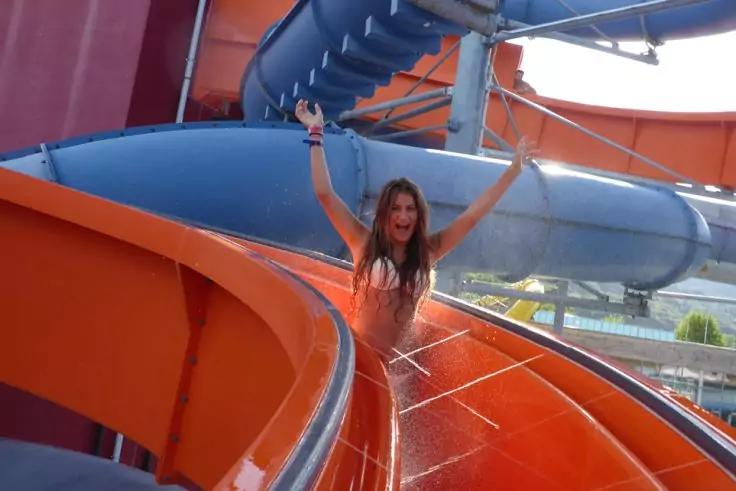 Frau im Bikini mit erhobenen Armen auf einer orange-blauen Wasserrutsche