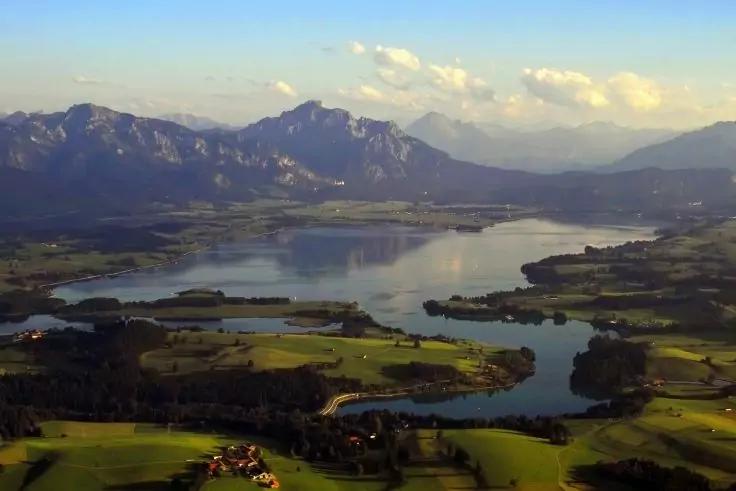 Gro&szlig;er See mit mehreren Inseln, gr&uuml;ne Wiesen im Vordergrund, Berge im Hintergrund, blauer Himmel mit vereinzelten Wolken