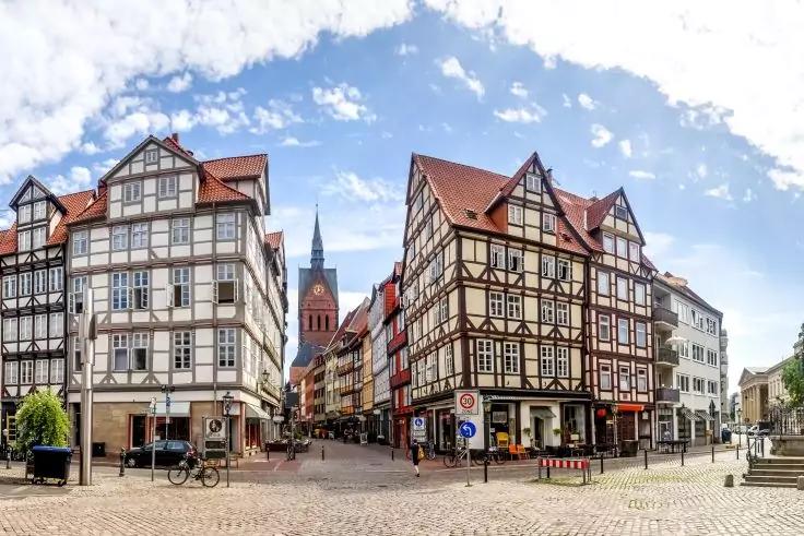 Marktplatz mit Fachwerkhäusern, Kopfsteinpflaster, schmale Straße in der Bildmitte, Kirchturm im Hintergrund, Fahrrad am Rand, blauer Himmel mit Wolken