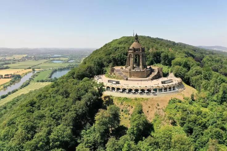 Großes steinernes Denkmal mit Kuppel auf bewaldetem Hügel, halbkreisförmige Terrasse und Fluss im Hintergrund unter klarem Himmel