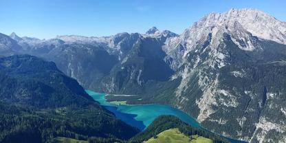 T&uuml;rkisblauer Bergsee zwischen steilen, bewaldeten H&auml;ngen und felsigen Gipfeln unter klarem blauem Himmel